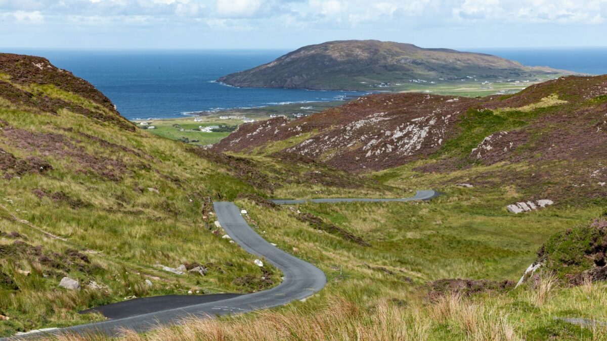 gray asphalt road on green mountain beside body of water during daytime